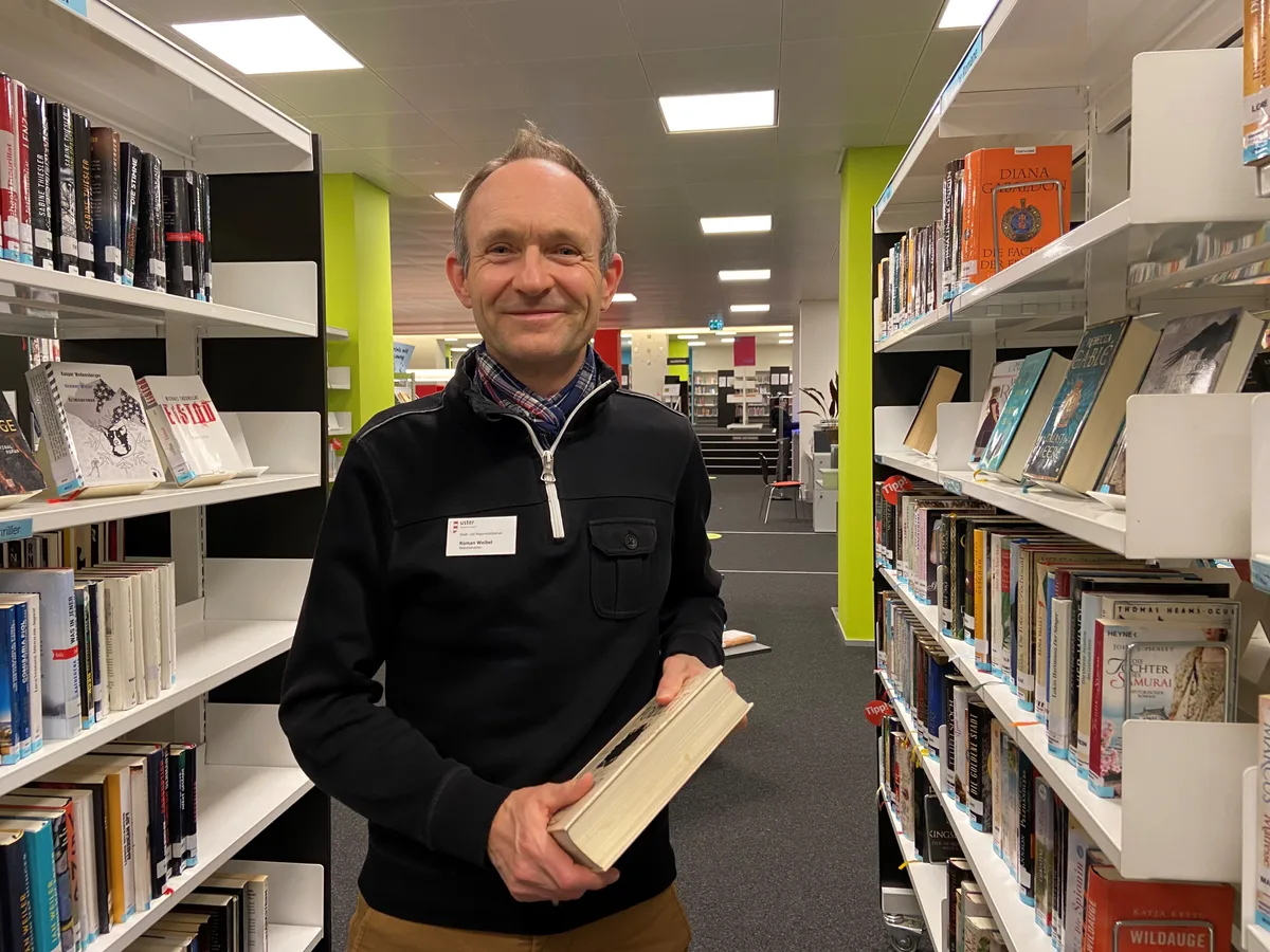 Bibliothekar mit Buch zwischen Gestell